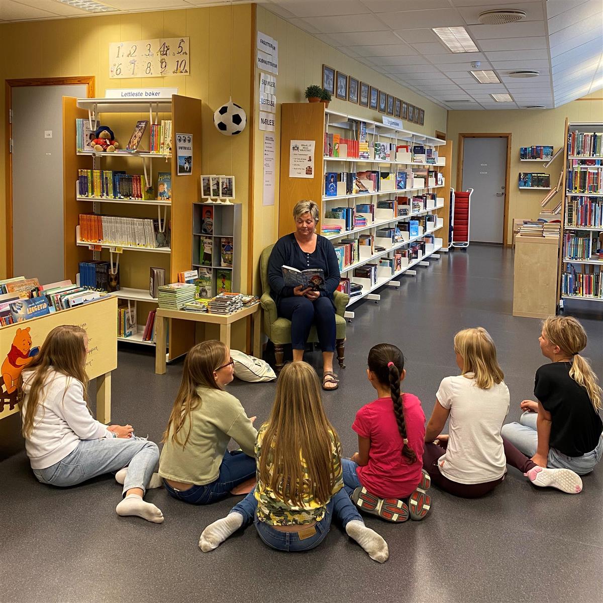 Bibliotekar leser høyt for barn i et bibliotek - Klikk for stort bilde