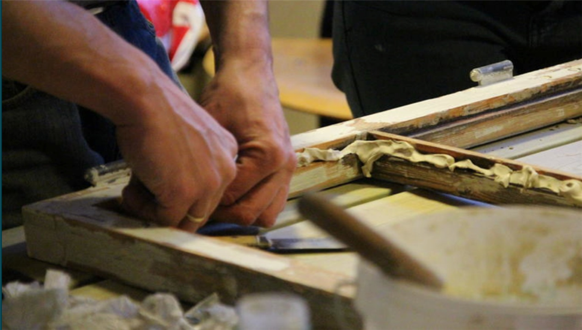 Rammen til et gammelt vindu i tre. To hender som arbeider med rammen. Fotografi