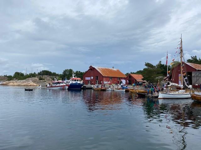 Utsikt fra båt mot brygge med rekker med båter liggende til kai på Bragdøya og med hovedhuset i sentrum- av bildet - Klikk for stort bilde